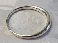 Smooth round sterling silver bangle bracelet shown from top view on light fabric surface.