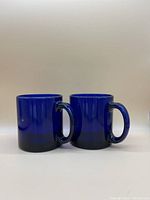 Two blue cobalt glass mugs front view on white background.