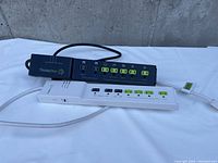 Two electrical extension cords with surge protectors; one black and one white, both with green outlet covers and individual switches.