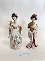 Two ceramic Geisha figurines, white kimonos with floral patterns, approximately 7 inches tall