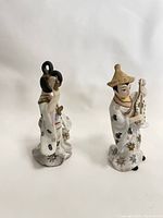 Side view of the two ceramic figurines highlighting detailed headwear and hand positions.