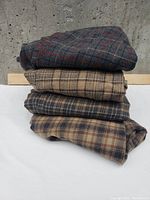 Stack of four folded plaid wool pants in various patterns and colors.