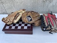 Four baseball gloves arranged next to wooden folding chess set