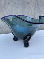 Front side view of the cobalt blue artisan glass bowl showing wavy rim, three legs, and internal crack visible inside the bowl.