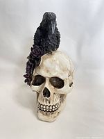 Front view of the skull figurine with crow and purple flowers on white background.