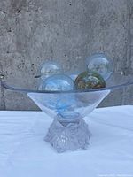 Front view of the clear glass bowl with flared rim and frosted rose base, showing the various clear, blue, and speckled glass spheres inside the bowl.