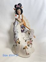 Front angle of white kimono porcelain geisha figurine holding fan, showing floral details and hairstyle