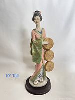 Front view of the porcelain geisha figurine on a round wooden base, showing pink kimono and green sash details, about 10 inches tall.