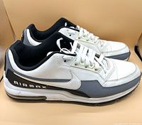 Side view of the right shoe showing white leather upper with grey and black accents, 'AIRMAX' branding on black heel panel, and visible air unit in sole.