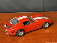 Side rear view of the red 1962 Ferrari GTO model car with white racing stripes on wooden surface