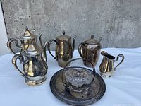 Photo of silver plated coffee pot, tea pot, sugar bowl, creamer, silver plated serving tray, and glass candy dish on white background.