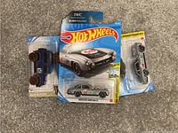 Photo showing three Hot Wheels cars in their original packaging: a blue Baja Blazers off-road vehicle, a silver and black Mercedes-Benz 300SL, and a silver sports car.