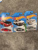 Photo showing three Hot Wheels die-cast cars in original blister card packaging. Cars are a red Nissan 300ZX, a silver Audi R8, and a silver Mercedes-Benz 600SEL.