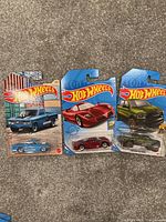Three Hot Wheels toy cars in original packaging displayed side by side on carpet surface.