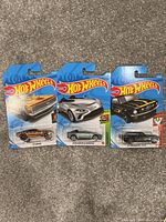 Three Hot Wheels toy car packages laid out on carpet including 67 Camaro, Aston Martin Red Lines, Mustang GT500 models.