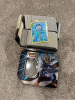 Photo of an open Pokémon collector tin featuring Empoleon artwork and a large stack of Pokémon cards including a holofoil Poliwhirl card on top.