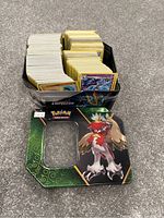Opened Pokémon tin with Empoleon on the base and Braviary on the lid, showing large collection of assorted Pokémon cards inside arranged upright