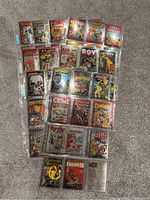 Photo of 28 individually sleeved chrome card prints of classic Golden Age comic book covers arranged on carpet.