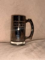 Photo of a shiny pewter mug engraved with 'Best Man' and decorative floral details, shown on a beige background.