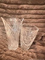 Both crystal vases side by side on brown textured fabric, showing size difference and detailed cut designs on each.