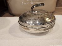 Closed round pickle dish with curved handle, silver-tone metal showing wear and tarnish.