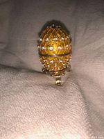 Front view of gold tone decorative Faberge inspired egg with clear rhinestones on surface, resting on mini stand.