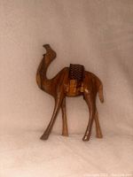 Front-facing photo of a small wooden camel figurine carved with detail and a woven saddle