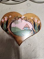 Top view of the heart-shaped wooden piece showing hand-painted floral and house scenery in pastel colors.