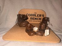 Full view of the four hand carved wooden boots on wooden base with backdrop labeled The Cobbler's Bench