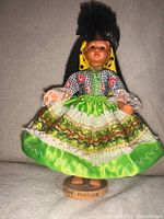 Front view of Nazare Portugal doll in traditional attire standing on a wooden base with 'Nazare - Portugal' label, showing details of vibrant skirt, lace, ribbons, and bonnet.