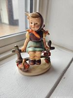 Front angled view of the porcelain figurine showing the girl sitting on a fence with basket