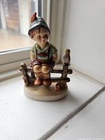 Front view of the Hummel figurine featuring a boy seated on a fence with a bird on the right side.