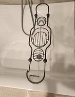 Metal bath caddy hanging in bathtub, showing oval and circular racks and hooks for holding bath items.