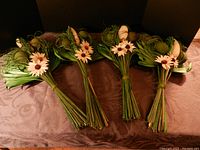 Four bundles of dried floral arrangements including palm leaves, seed pods, and wood faux flowers arranged side-by-side on dark fabric.