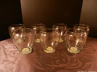 Seven clear glass candle holders arranged on a table with a patterned cloth, viewed from the front