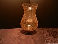 Side view of gold-tinted crackle glass candle holder standing on patterned fabric under warm lighting