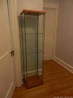 Full view of the IKEA Detolf glass display cabinet showing pine wood top and bottom, three glass shelves inside, and clear glass sides and door.