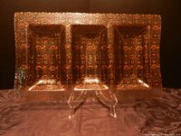 Front view of decorative glass serving platter with gold painted intricate patterns in three sections on a display stand.