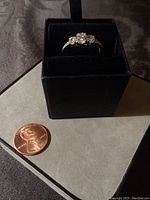 Diamond Aura Dearly Beloved ring displayed in a black velvet ring box beside a US penny for scale, showing the ring's three-stone setting and overall condition.