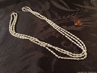 Full view of the 3-strand necklace showing the lengths and combined white and gold beads on black fabric background.