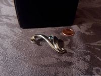 Front view of silver-tone abstract brooch with blue stone beside penny for scale