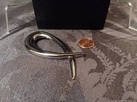 Top front view of silver tone abstract swirl brooch next to a penny for scale