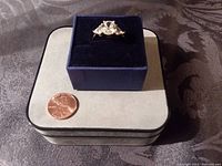 Photo of a vintage silvertone cocktail ring with three clear crystal stones displayed on a navy blue velvet ring box, with a penny for size reference.