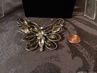 Butterfly silvertone metal brooch with crystal and smoked glass bead accents shown next to penny for scale.