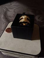 Goldtone cocktail ring displayed upright on black jewelry box with penny nearby for size scale.