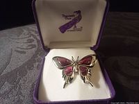 Butterfly pin in original purple presentation box, angled view showing front and right side with mauve enamel wings and silvertone metal body.