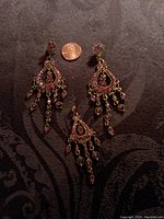 Goldtone chandelier style earrings and matching pendant lying on fabric beside a penny for scale, showing pink stones and intricate metalwork.