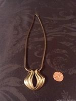 Full view of goldtone necklace with pendant on a dark fabric background alongside a penny for size reference.