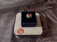 Photo of the adjustable silvertone cocktail ring displayed in a small velvet box next to a penny for size comparison.