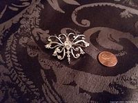 Front view of silvertone butterfly pin with white crystal stones next to a penny for size reference.